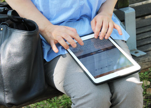 公園のベンチに座り、iPad Airで介護支援記録を入力するケアマネジャーの方