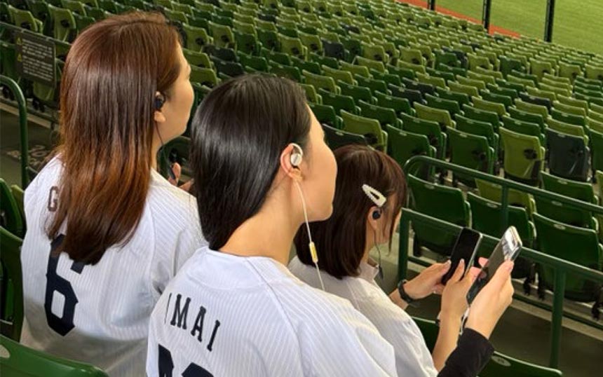 実証実験のイメージ。「耳スピ」を装着した女性が球場のスタンドで観戦する様子