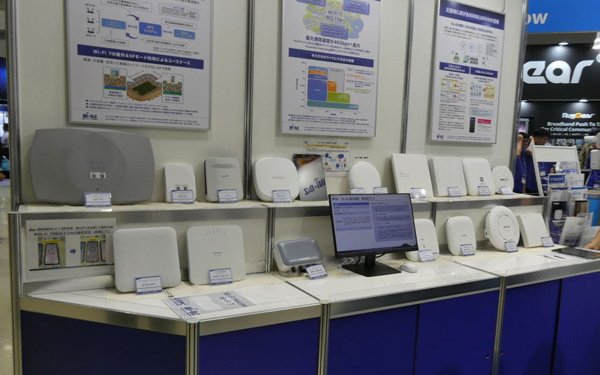 Exhibition booth displaying a range of white wireless networking devices and routers with posters behind them in the background.