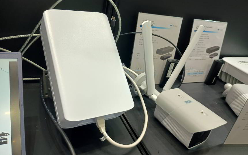 White wireless router with two antennas and cables on a retail display, with product boxes in the background.