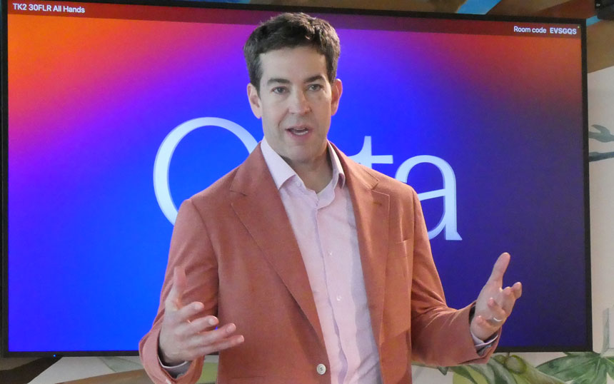 Man in an orange blazer and pink shirt giving a presentation in front of a gradient screen.