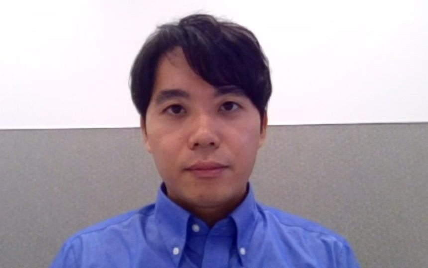 Head-and-shoulders portrait of a man in a blue button-down shirt looking at the camera with a neutral expression in an office setting.