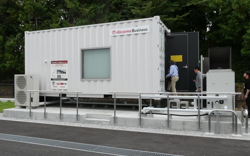 NTTドコモビジネス横浜第1データセンターの敷地内に設置されたコンテナ型データセンターショールームの外観。同型のコンテナをコンテナDCパークで利用する。窓は見学用のため実際には設けない。右側の縦型の装置が液冷用のチラー