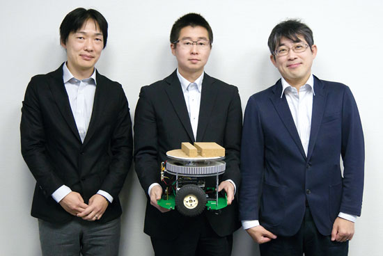 （左から）NEC 中央研究所 システムプラットフォーム研究所 主任研究員 吉田裕志氏、同研究所 スマートコミュニケーションTG 熊谷太一氏、同研究所 部長 里田浩三氏。熊谷氏が手に持っているのがAGVのプロトタイプ